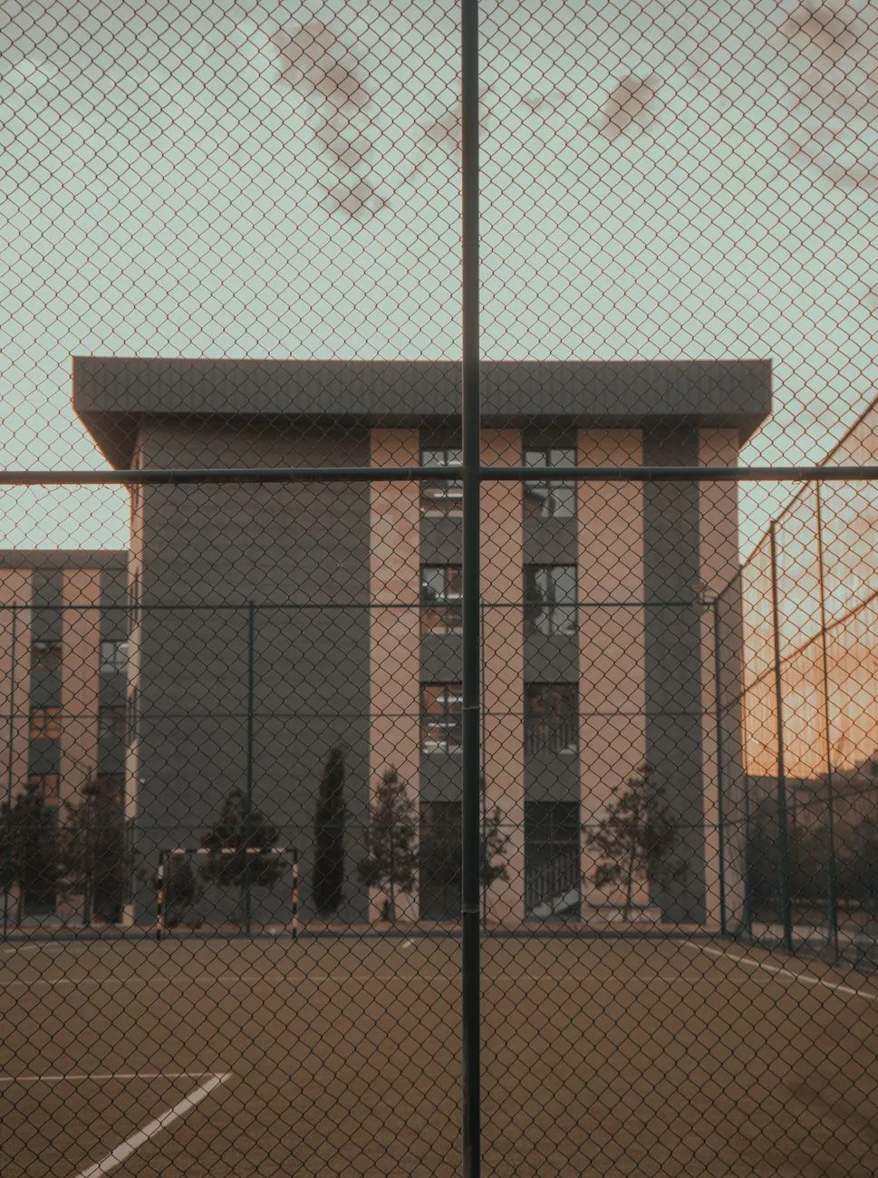 Exterior view of a modern school building with a fenced soccer field at dusk.